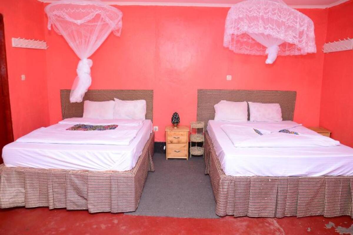 Een kamer met twee bedden, elk met een witte spreidek en bijpassende hoofdborden. Daartussen staat een klein houten nachtkastje, met erboven een enkele hanglamp.