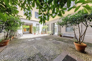Un patio con plantas en macetas, piso de adoquines y la entrada de un edificio.