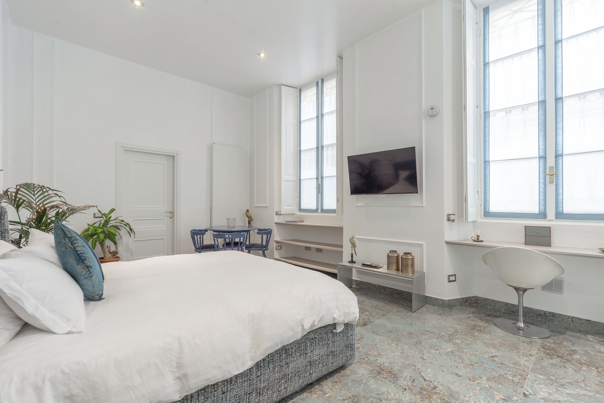 A bedroom with a large bed, a desk, a chair, a TV, and a window.