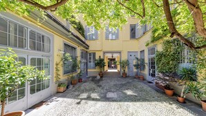 A courtyard with a cobblestone floor, potted plants, and a building with large windows and shutters. - Duomo Smart Suites (Milan)