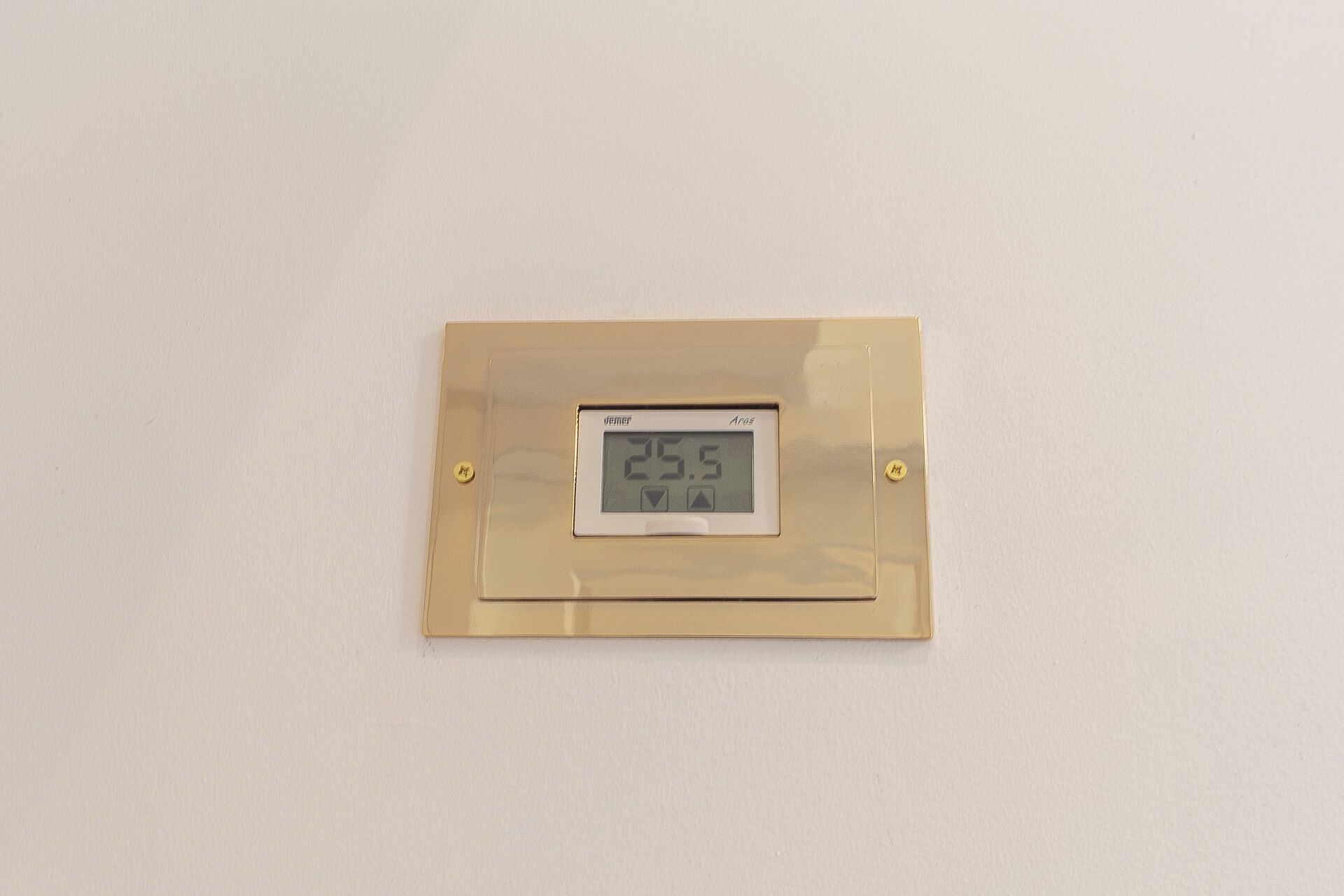 A thermostat mounted on a wall with a digital display showing 25.5 degrees.