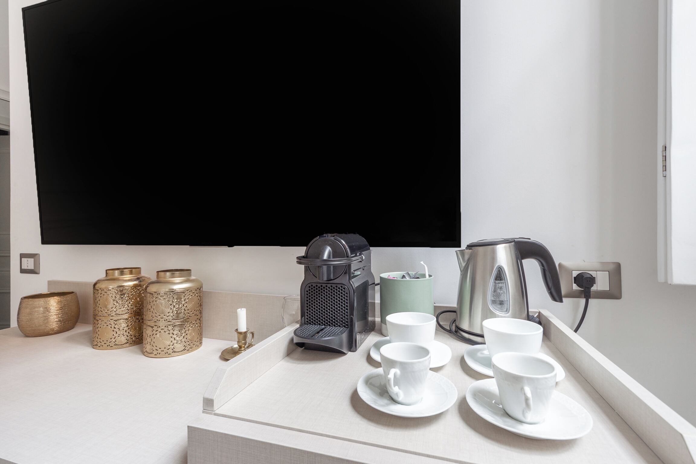 A kitchen counter with a coffee maker, two cups, a kettle, and decorative containers.