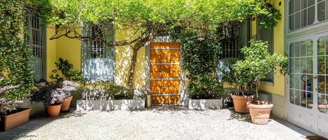 Un patio con suelo de baldosas, una verja de madera y macetas con plantas.