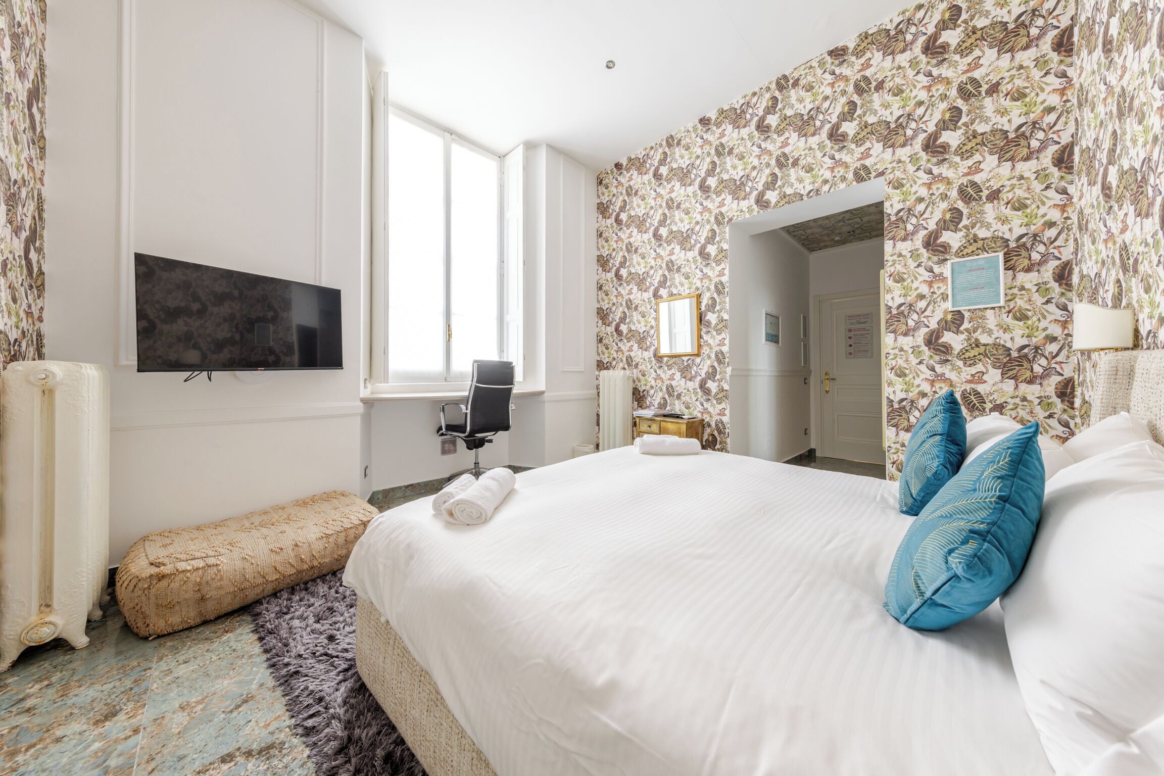 A hotel room with a large bed, a flat-screen TV, a chair, a small table, and a window.