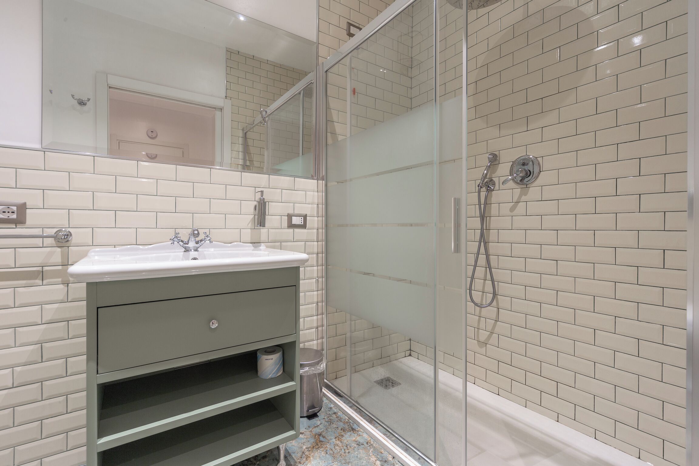 A modern bathroom with a glass-enclosed shower, white subway tiles, a sink with a mirror, and a green vanity.