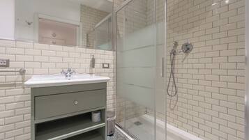 A modern bathroom with a glass-enclosed shower, white subway tiles, a sink with a mirror, and a green vanity.