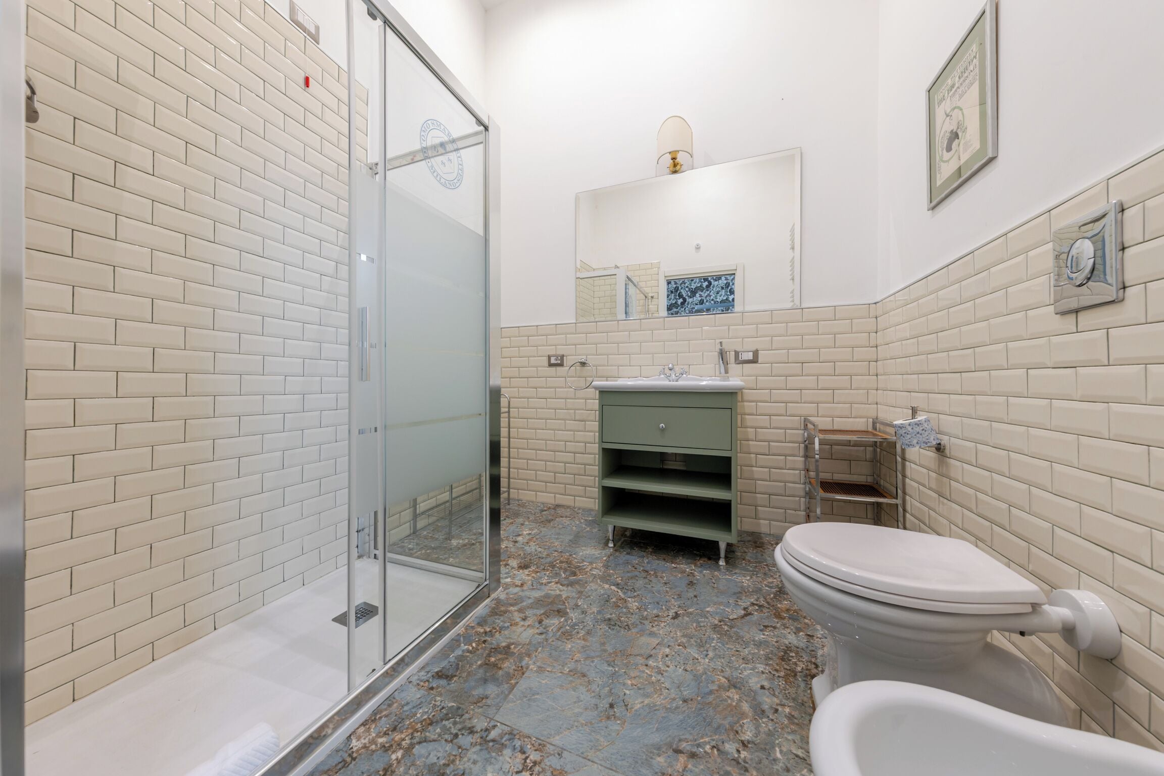 A bathroom with a glass shower enclosure, a toilet, a sink with a mirror above, and a tiled floor.