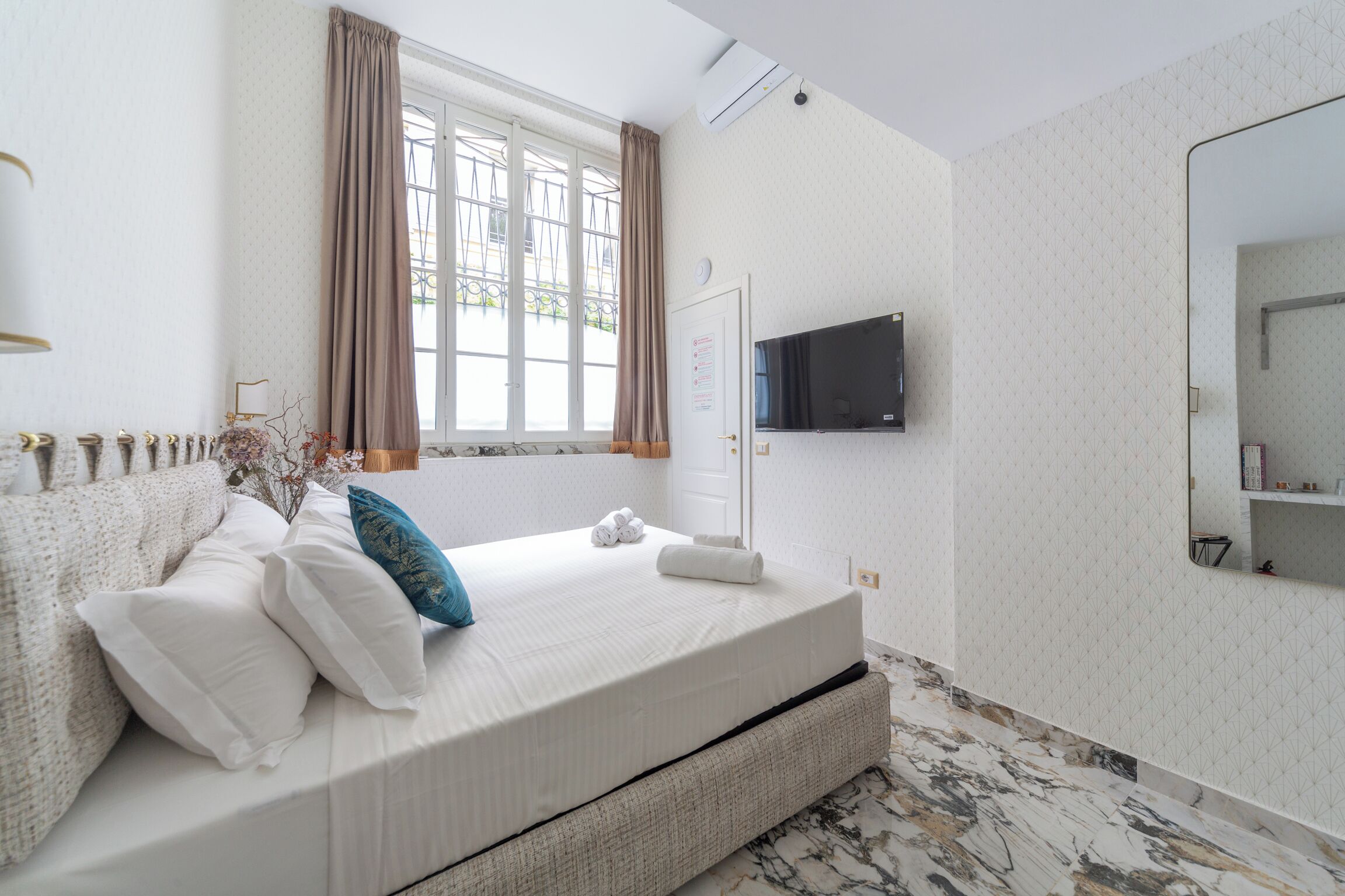 Une chambre d’hôtel avec un lit, une télévision, une fenêtre avec des rideaux et une salle de bain avec un miroir.