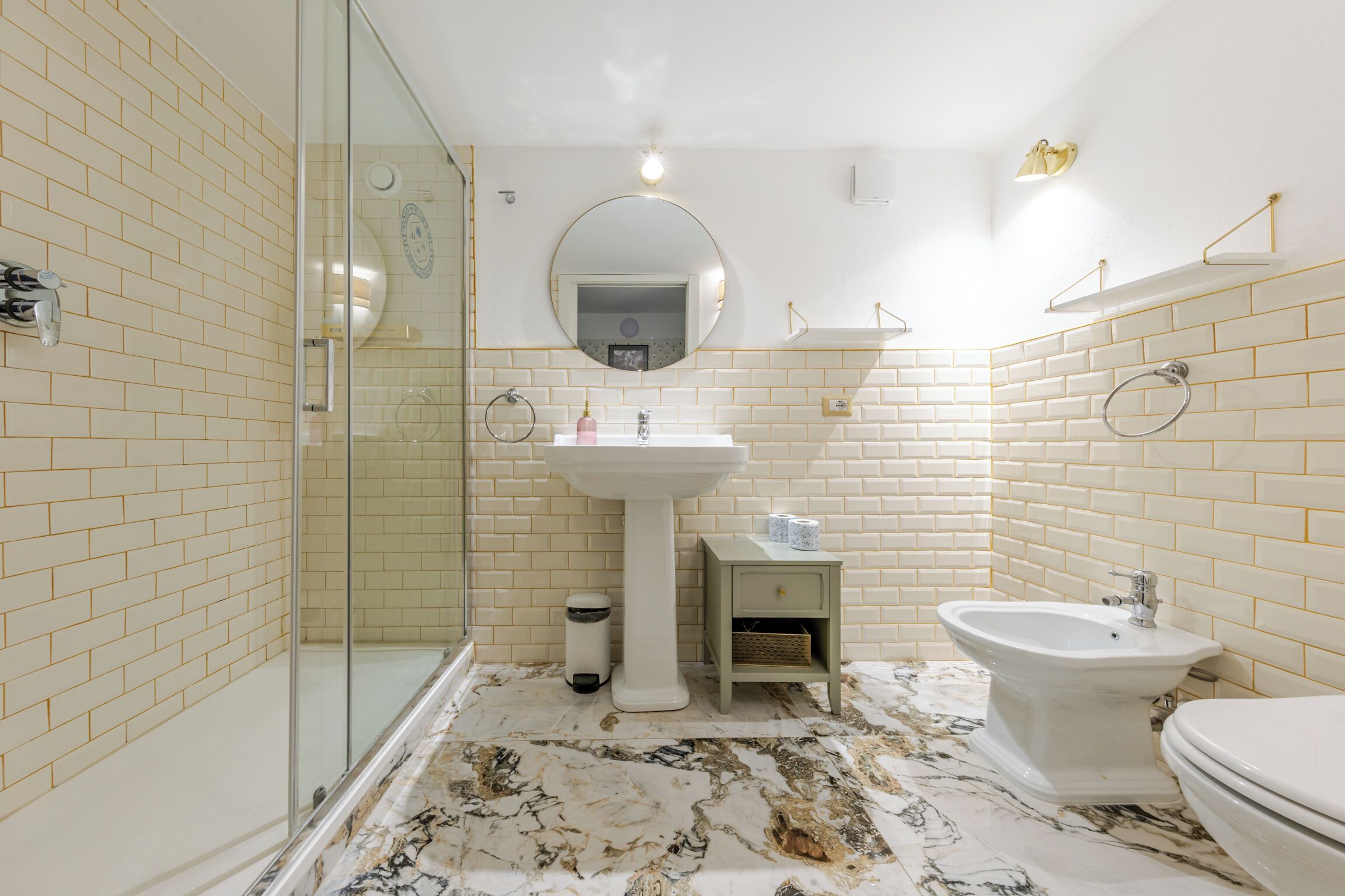 Une salle de bain avec une douche à parois de verre, un lavabo sur colonne, un bidet et des toilettes.