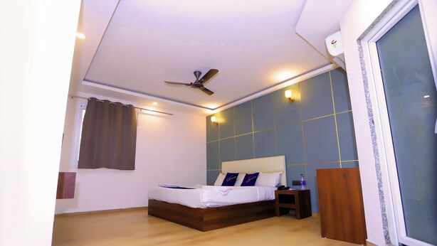 Un dormitorio con cama, ventilador de techo, mesita de noche y ventana con cortinas.