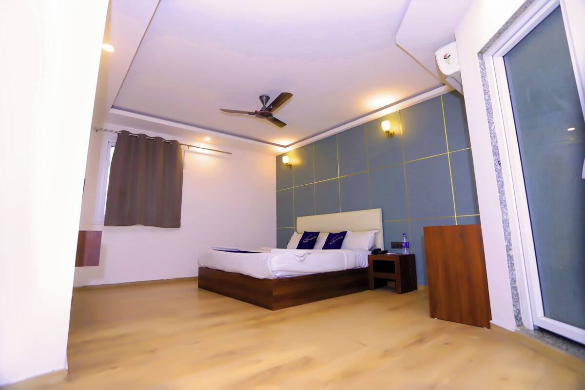 Un dormitorio con cama, ventilador de techo, mesita de noche y ventana con cortinas.