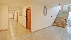 Un pasillo amplio con suelo de piedra pulida, puertas de madera y una escalera con barandilla de metal.