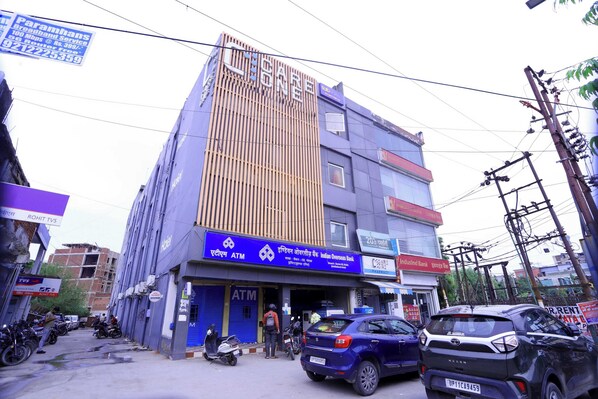 A multi-story building with an ATM on the ground floor, a sign for Indian Overseas Bank, and several parked vehicles.