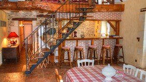 Una cocina rústica con una escalera de madera, un comedor con mantel a cuadros y una barra con taburetes.