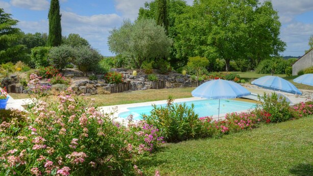 Un jard ín trasero con piscina, rodeado de abundante vegetación y plantas en flor.