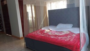 A bedroom with a bed covered by a canopy, a red bedspread, and a dark headboard. - Charming House in Matugga, Kampala, Uganda (Matugga)