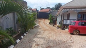 A paved driveway leading to a house with a red car parked on the right. - Charming House in Matugga, Kampala, Uganda (Matugga)