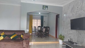 A living room with a sofa, a dining table with chairs, a TV, and a potted plant. - Charming House in Matugga, Kampala, Uganda (Matugga)