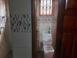 A bathroom with a shower, toilet, and a window with bars.