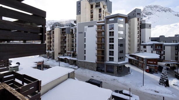 Un hotel moderno con varios pisos, balcones y un paisaje nevado de montañas.