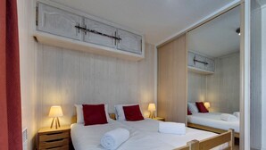 Habitación de hotel con dos camas, cabeceros de madera, ropa de cama blanca, almohadas rojas, lámparas de noche y un espejo grande.