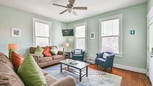 A living room with a ceiling fan, two sofas, a coffee table, and a TV. - Coastal Blue Cottage is Steps to Beach and Seawall (Galveston)