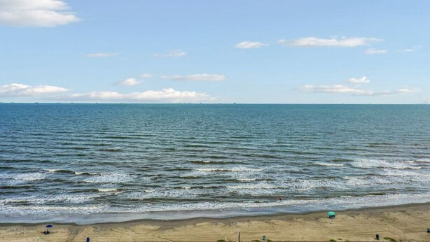 A beach with waves, a clear sky, and distant land. - Coastal Blue Cottage is Steps to Beach and Seawall (Galveston)