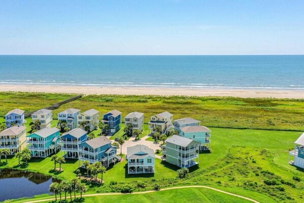 A coastal residential area with multiple two-story houses, a beach in the background, and a small body of water in the foreground.