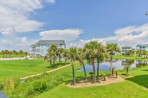 A large, two-story building with a light blue exterior and a grey roof, surrounded by a well-maintained lawn and palm trees.