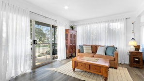 Relax in this inviting living space with a comfortable sofa, wooden coffee table, and sliding glass door leading to an outdoor area.