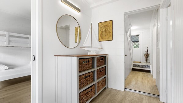 Un couloir avec un mur blanc, un miroir, une carte encadrée et des paniers en osier sur une étagère.