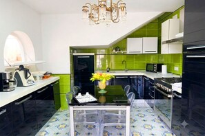 Una cocina moderna con comedor, que presenta una araña, salpicadero de azulejos verdes y una mesa de vidrio transparente.