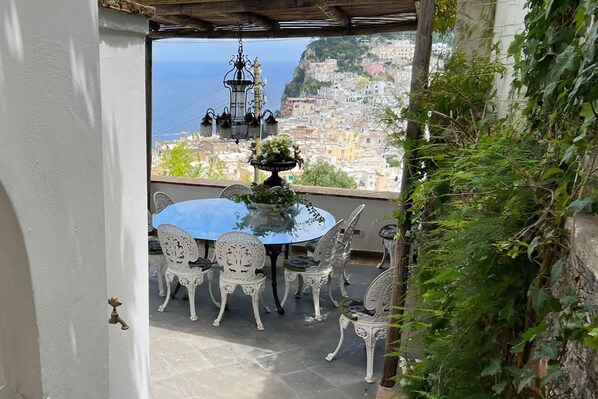Un espacio exterior para comer con una mesa y sillas, vista a una ciudad costera y un farol decorativo.