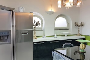 Una cocina moderna con un refrigerador de acero inoxidable, dispensador de agua integrado y una encimera negra con un lavamanos blanco.
