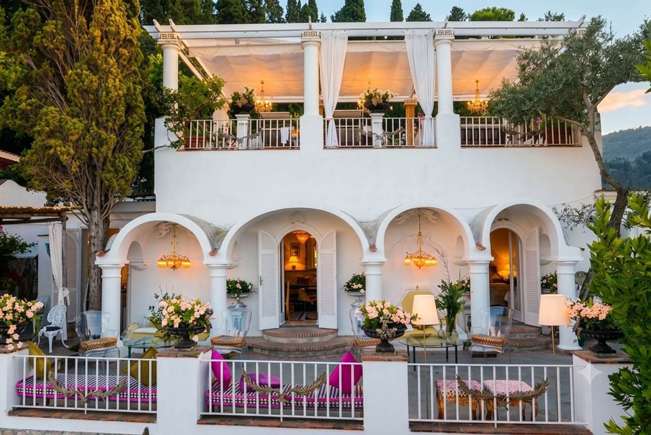 A two-story building with a balcony, arched doorways, and outdoor seating with cushions.