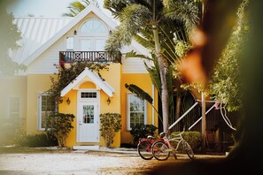 A yellow house with a white door, a balcony, and two bicycles parked in front.