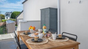 A wooden table set with breakfast items, including pastries, fruit, and juice, on a balcony with a view of a residential area. - Le Clos Moguer by Interhome (Quiberon)