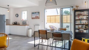 A modern kitchen with white cabinets, a dining area with a table set for two, and a bookshelf filled with books. - Le Clos Moguer by Interhome (Quiberon)