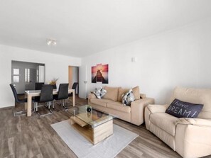 Una sala moderna con una mesa de centro de vidrio, un sofá color beige y un comedor con una mesa y sillas de vidrio.