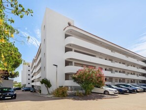 Un hotel de varios pisos con fachada blanca, balcones y un estacionamiento con varios automóviles.