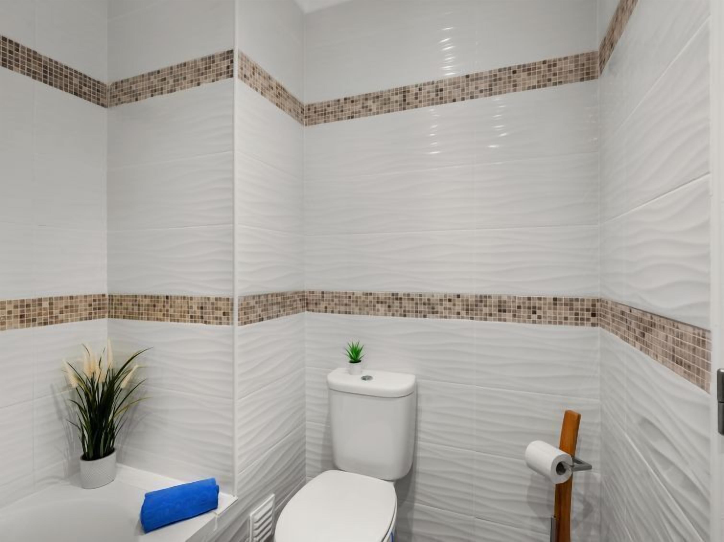 A bathroom with white tiles, a toilet, a small plant, and a blue towel.