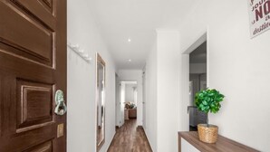 Un couloir avec une porte en bois, une plante en pot et un tableau encadré accroché au mur.