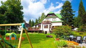 Ein Haus mit einem grünen Dach, einer Holzterrasse und einer Schaukel im Garten.