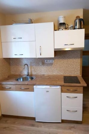 A compact kitchen with white cabinets, a stainless steel sink, a coffee maker, and a compact dishwasher.