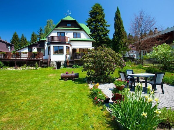 A two-story house with a green roof, a balcony, and a well-maintained garden with a patio area.