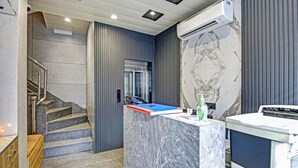 Un hall d’hôtel moderne avec un comptoir d’accueil en marbre, un escalier et un appareil de climatisation.