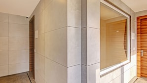 Une salle de bain moderne avec de grands murs recouverts de carreaux, une porte en bois et une cabine de douche en verre.