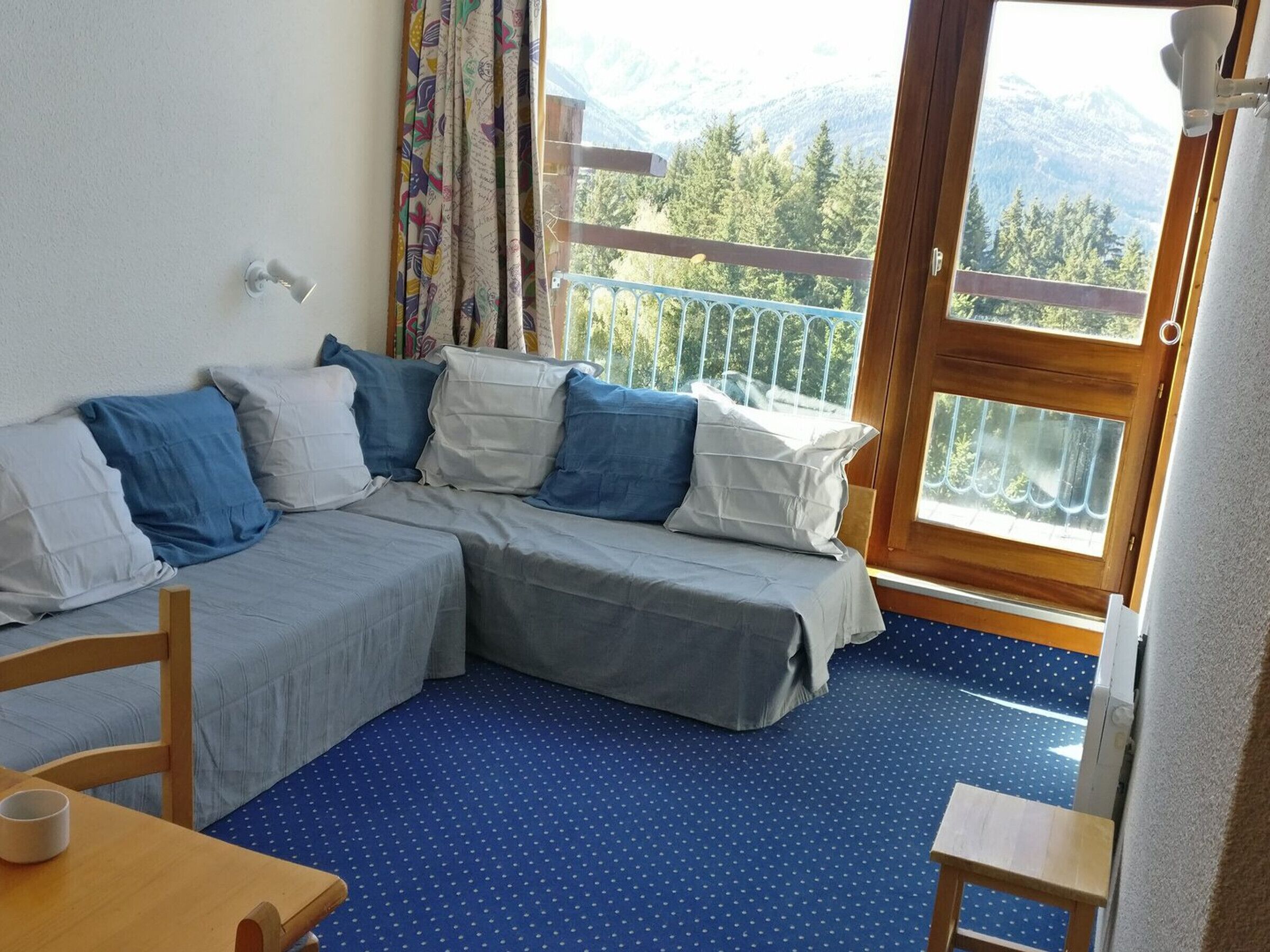 A room with a bed, a table, and a view of mountains through a balcony.