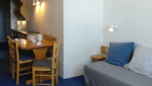 A small, cozy room with a wooden dining table and chairs, a small stool, a bed with a grey blanket, and a wall-mounted light fixture. - Studio 4 pers · Ski-in/Ski-out · Balcony (Les Arcs 1800)