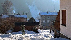 A snow-covered courtyard with buildings, a wooden fence, and a small tree. - Rieger 4 by Interhome (Harrachov)